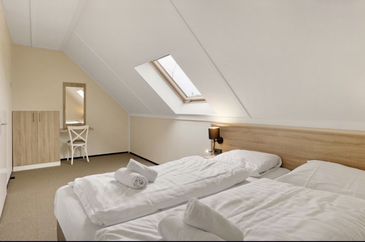 Ruime slaapkamer met witte lakens en opgerolde handdoeken